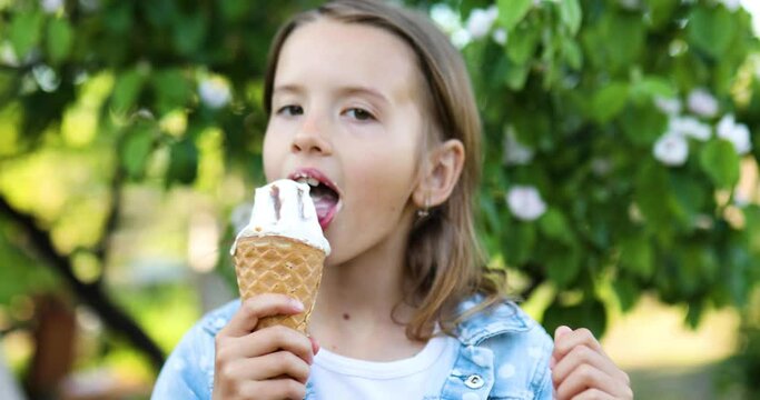 Cute girl with italian ice cream cone smiling and looking at camera while resting in park on summer day, child enjoying ice cream outdoor, happy holidays, summertime