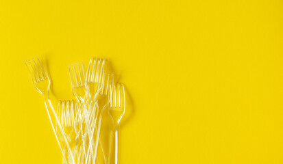 Much transparent disposable plastic forks on vibrant yellow background, top view. Flat lay...