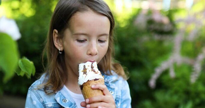 Cute girl with italian ice cream cone smiling and looking at camera while resting in park on summer day, child enjoying ice cream outdoor, happy holidays, summertime