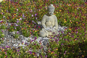 Decorative buddha statue in a flower garden of pansies.