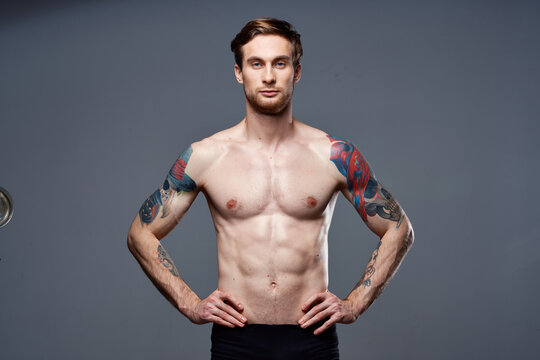 handsome man with a naked pumped-up torso tattoos on his arms holds his hands on his belt