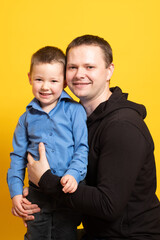 Cheerful happy father with baby boy playing. Young dad with his son laugh and smile on a yellow background. Family concept.
