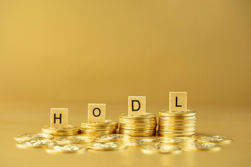 HODL written on wooden blocks on stack of bitcoins on golden background. Acronym standing for 'hold on for dear life' in cryptocurrency concept.