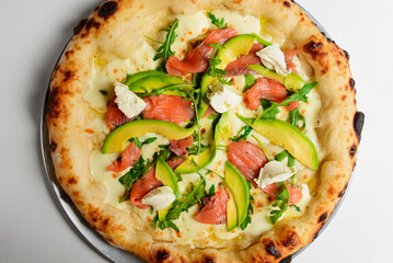 Delicious pizza with salmon, cheese, avocado and fresh arugula. Over white background.