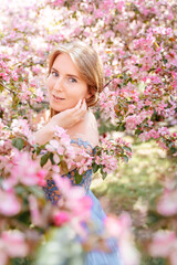 Portrait of a young woman with natural white skin with red hair, against the background of a cherry rose garden. A dreamy girl in a spring park. Allergy free concept.