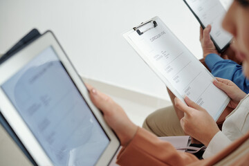 Job candidates sitting in office corridor and filling cv forms before interview with human...