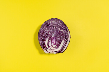 Half of purple cabbage head with shadow on yellow color with copy space, top view. Simple food...