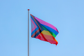Progress pride flag (new design of rainbow flag) waving in the air with blue sky, Celebration of...