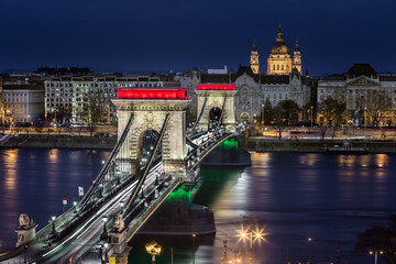 Fototapeta na wymiar Budapest, Hungary - The world famous illuminated Szechenyi Chain Bridge (Lanchid) by night, lit up with national red, white and green colors with St.Stephen's Basilica at background on revolution day
