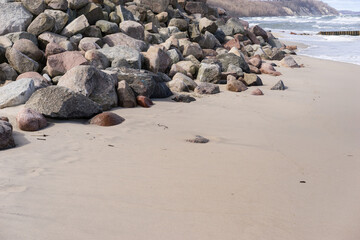 Fototapeta na wymiar Stones laying down on the sandy beach in the water waves and sea foam