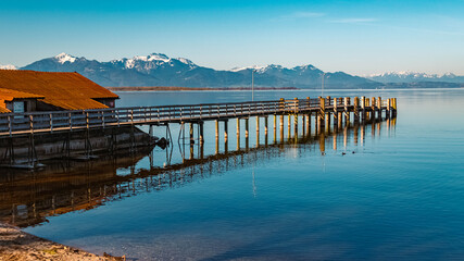 Obraz premium Beautiful alpine spring morning view with reflections, details of a pier and the alps in the background at the famous Chiemsee, Chieming, Chiemgau, Bavaria, Germany