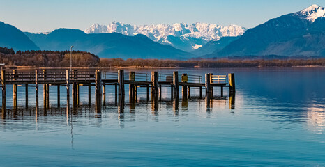 Beautiful alpine spring morning view with reflections, details of a pier and the alps in the background at the famous Chiemsee, Chieming, Chiemgau, Bavaria, Germany