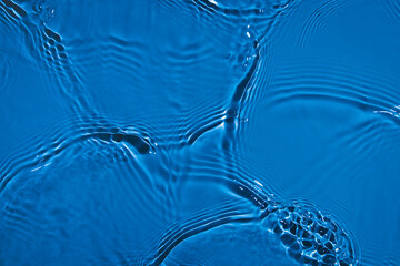 De-focused transparent dark blue colored clear calm water surface texture with splashes and...