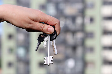 House purchase, real estate agent holding house key on background of new buildings. Moving home or renting property