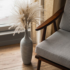 Mid-century retro chair and pampas grass bouquet in clay pot against window with curtains. Modern...
