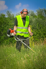 Worker mowing grass with grass trimmer
