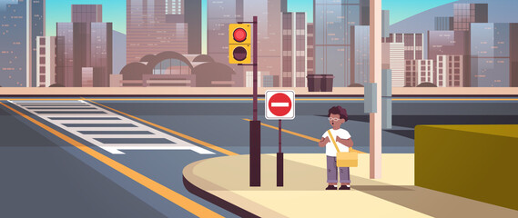african american schoolboy with backpack standing on city street near red stop road sign road safety concept cityscape
