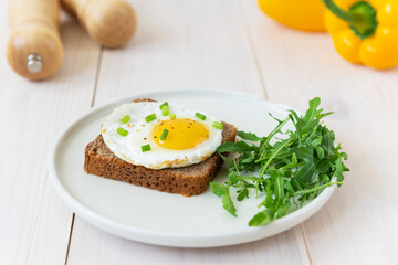 Toast with fried eggs with green onions, arugula and spices in a plate on a wooden table.