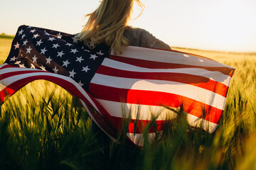  Happy young woman holding American flag at sunset.  4th of July.  Independence Day.