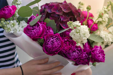 Very nice young woman holding big and beautiful bouquet of fresh hydrangea, roses, eucalyptus flowers in pink and purple colors, cropped photo, bouquet close up