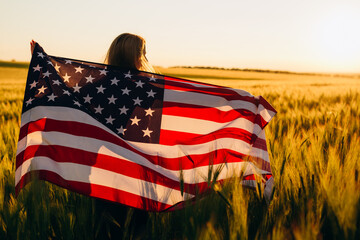 Beautiful young  girl with the American flag in a wheat field at sunset. 4th of July. Independence Day.	