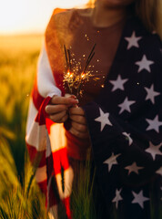 Young woman holding bengal fire with American flag at sunset. America celebrate 4th of July....