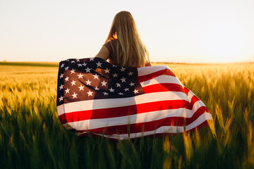 Beautiful young  girl with the American flag in a wheat field at sunset. 4th of July. Independence Day.	