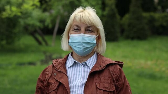 Coronavirus 19 protective mask against dangerous diseases, allergies and viruses. Adult senora 50 years old woman in a surgical mask looking at the camera in a summer park. Healthcare.