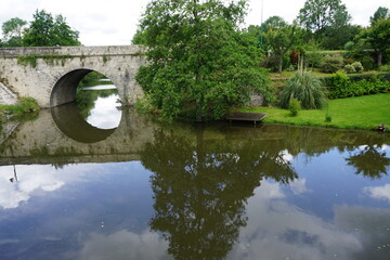 Fototapeta na wymiar mirror reflection of an old stone bridge and trees in the river in Vendée, france