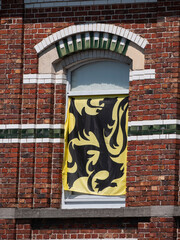 The Flemish flag, yellow with a black Flemish lion in front of a window of a house