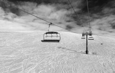 Black and white snowy off-piste ski slope, chair-lift on ski resort and sky with clouds