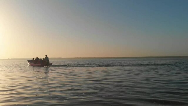 Silhouette Of Speedboat With Passengers Going Past On Keenjhar Lake  During Golden Hour. Aerial Pedestal Up