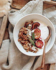 Granola with roasted plums and sage leaves on wooden tray with linen napkin