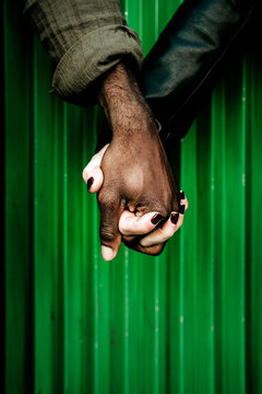 Cropped Image Of Couple Holding Hands Against Green Corrugated Iron