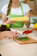 Unknown young woman slicing greens for a delicious fresh vegetarian salad while sitting and smiling at the kitchen desk, just hands, close-up. Cooking concept