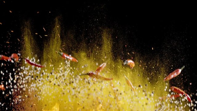 Mixture of ground spices, assorted peppers, salt and small red chili peppers slowly rise and fall against a black background. 300fps