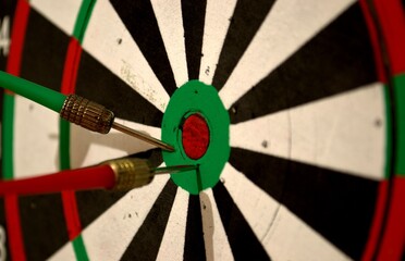 Colored darts on the wall. The target has two darts red and green
