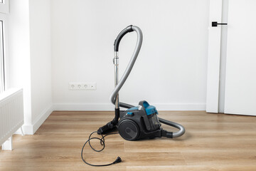 Modern blue vacuum cleaner on the wooden floor in living room.