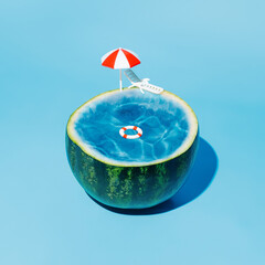 Watermelon as a pool with crystal clear blue water, parasol, swimming ring, and sunbed on a blue...