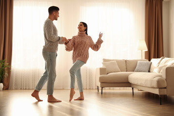Happy couple dancing barefoot in living room. Floor heating system