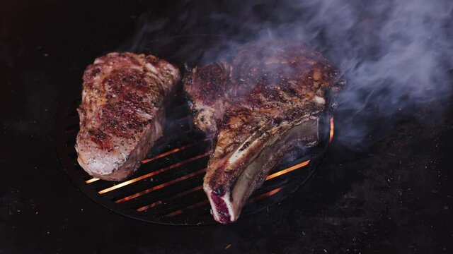 Rib eye steaks with spices on a barbecue grill grate with a blazing fire. Slow camera rotation. 4K slow motion.