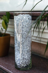 An elegant glass vase with glass ice cubes on table. A part of interior of modern cafe in loft style. Vertical photo