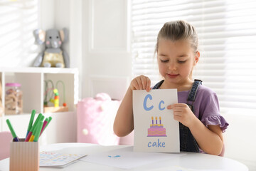 Little girl holding card with letter C and word Cake in classroom at English lesson