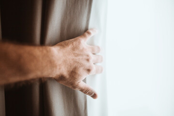 A new day through an open window - a male hand opens a thick curtain letting bright sunlight into the room