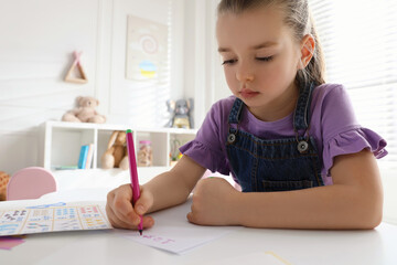 Little girl writing numbers in classroom at English lesson