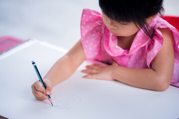 Selective focus of 4 year old girl holding pencil drawing cartoon on big paper on desk. Hobby of children. Kid learning at home. Home school. Small class.