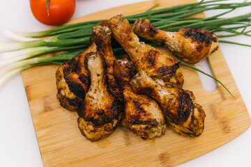 Fried chicken legs lie on a wooden board. Chicken shish kebab with a side dish of vegetables and green onions.