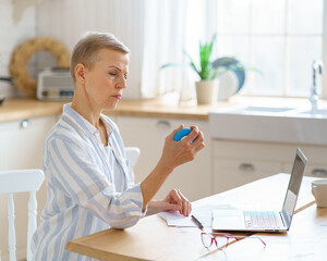 Focused mature woman exercising with rubber round grip ring for palms while working or studying on...