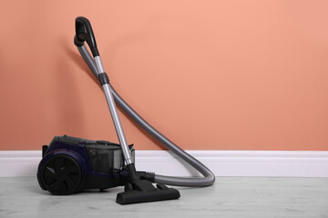 Modern vacuum cleaner on floor near orange wall indoors. Space for text