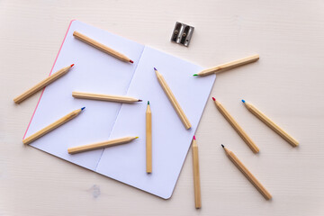 Open white notebook, with colored crayons beside it, penknife and drawing of a colored flower. 